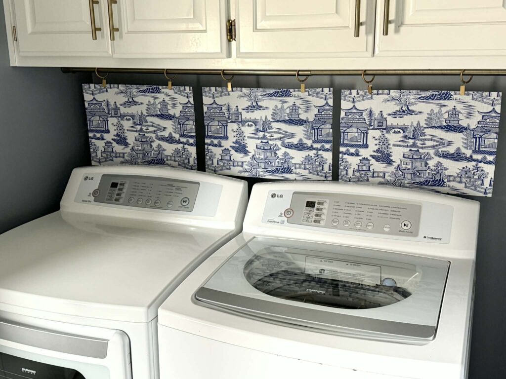 Blue and white placemat curtain on a tension covering the washer dryer hookups and outlets in a laundry room.
