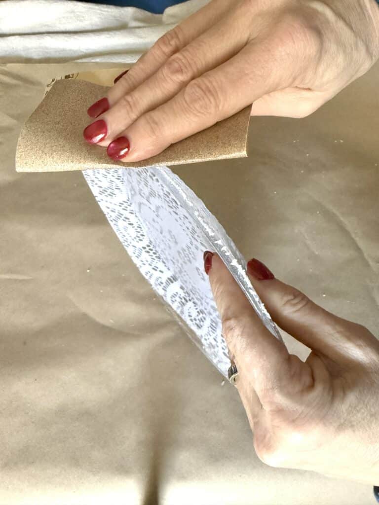 Sanding the rim of a plate covered with decoupage lace.