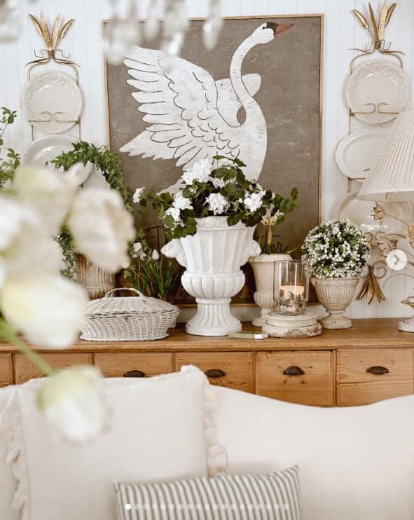 Vignette consisting of a white bird art piece, white vases, and white flowers.