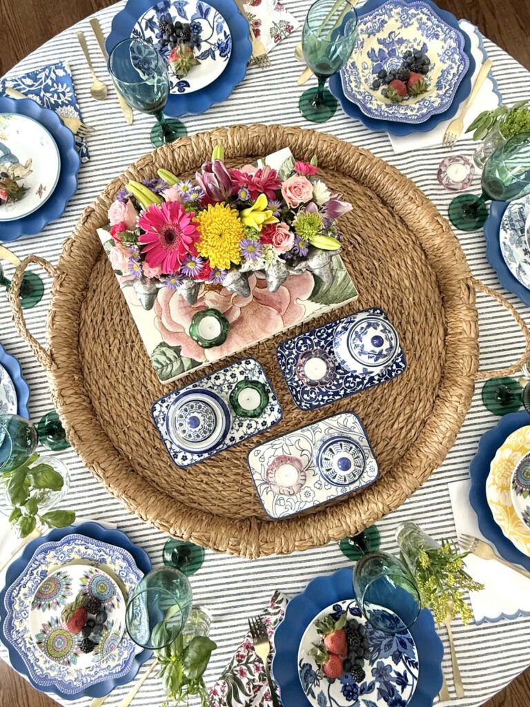 a grandmillennial style table setting with vintage plates, woven tray, and fresh flowers.