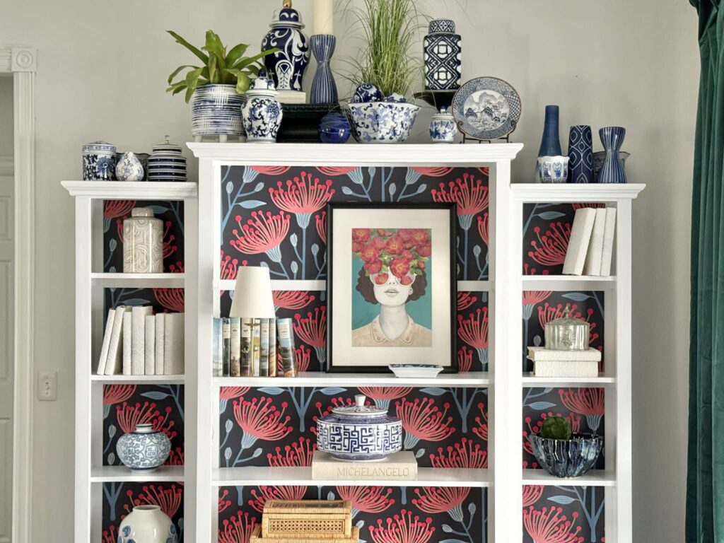 Bookshelves decorated in grandmillennial style with blue and white chinoiserie, artwork, woven boxes, and white covred books.