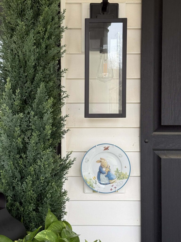 A bunny patterned plate hanging on the front of the porch under a light sconce.