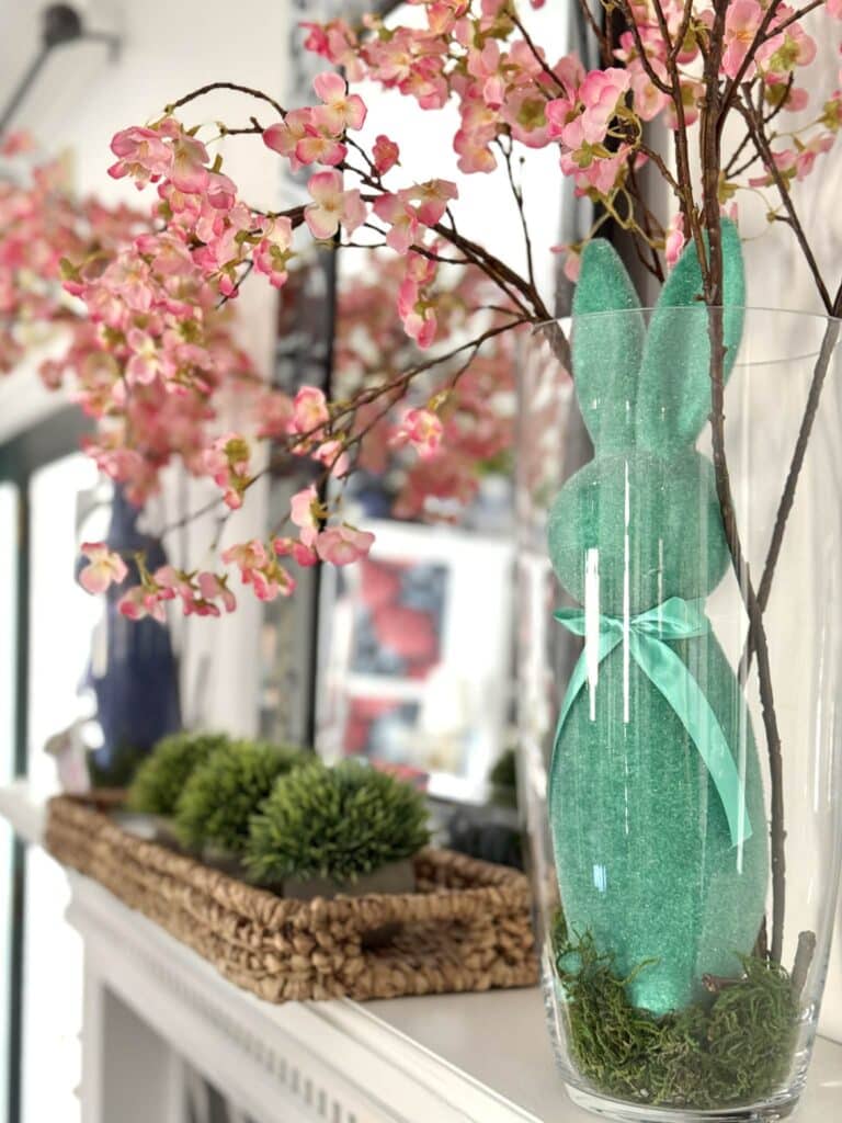 A green flocked bunny in a glass vase with cherry blossoms spilling out the top.