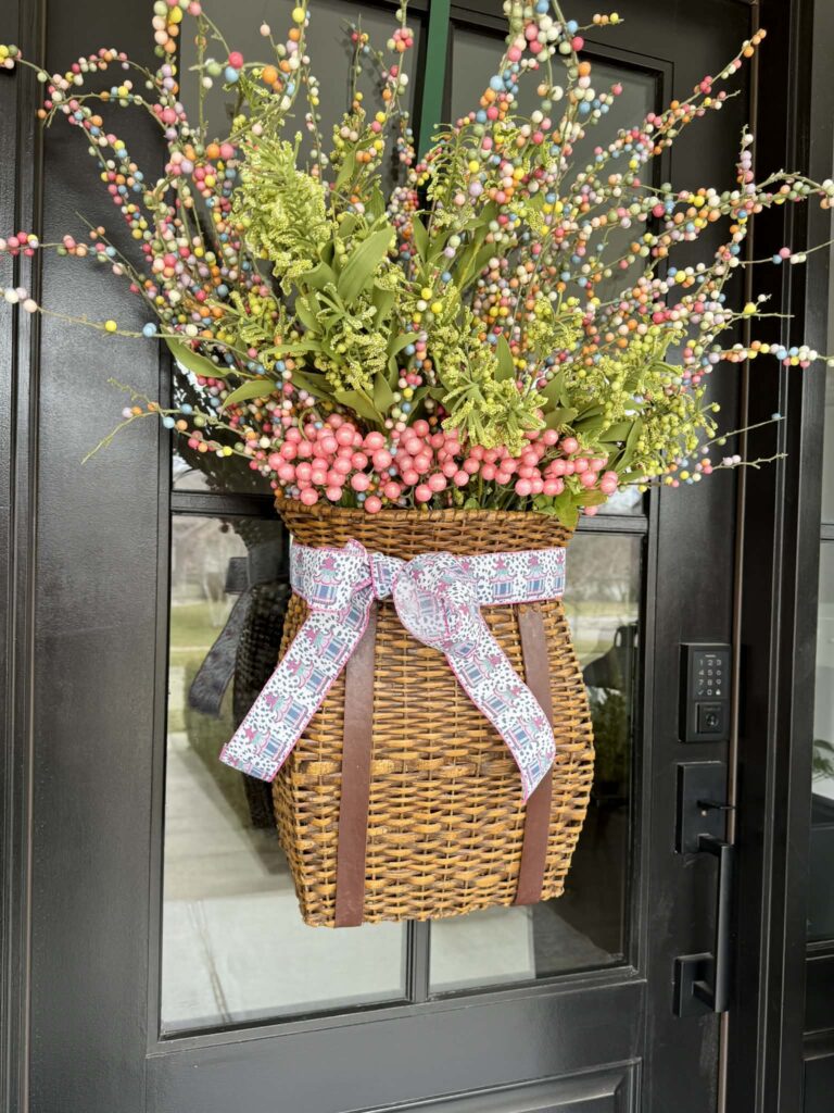 A hanging door basket filled with greenery, tall pip berry stems, and wrapped in a chinoiserie ribbon.