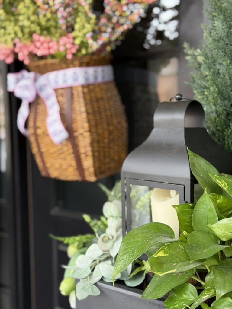 A black lantern nestled into a porch planter filled with a green plant.