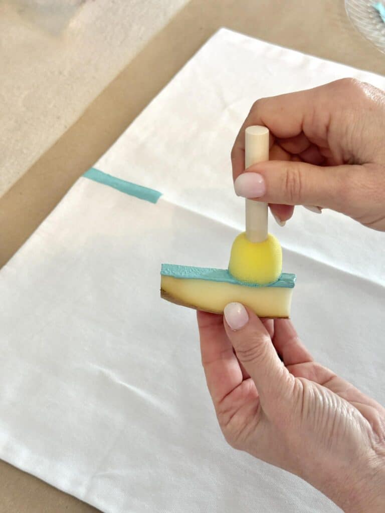 Applying light blue paint to a piece of potato for block printing.