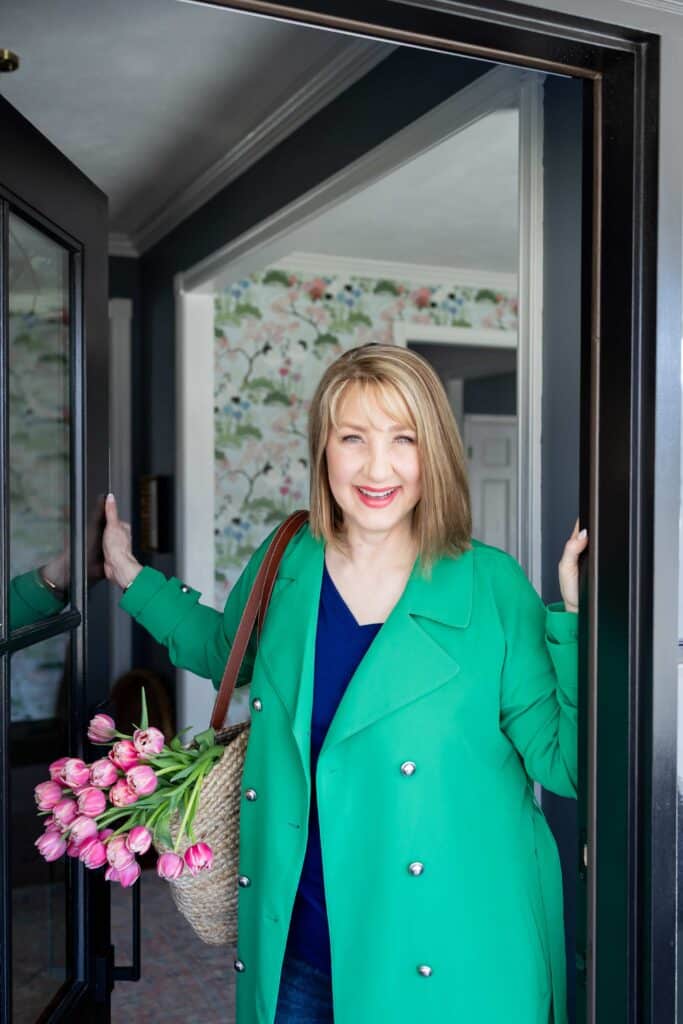 A woman in a green coat with a woven bag filled with pink tulips.
