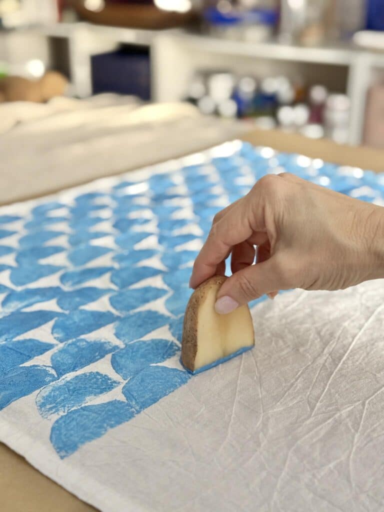 Block printing a pattern on a tea towel with a potato block.