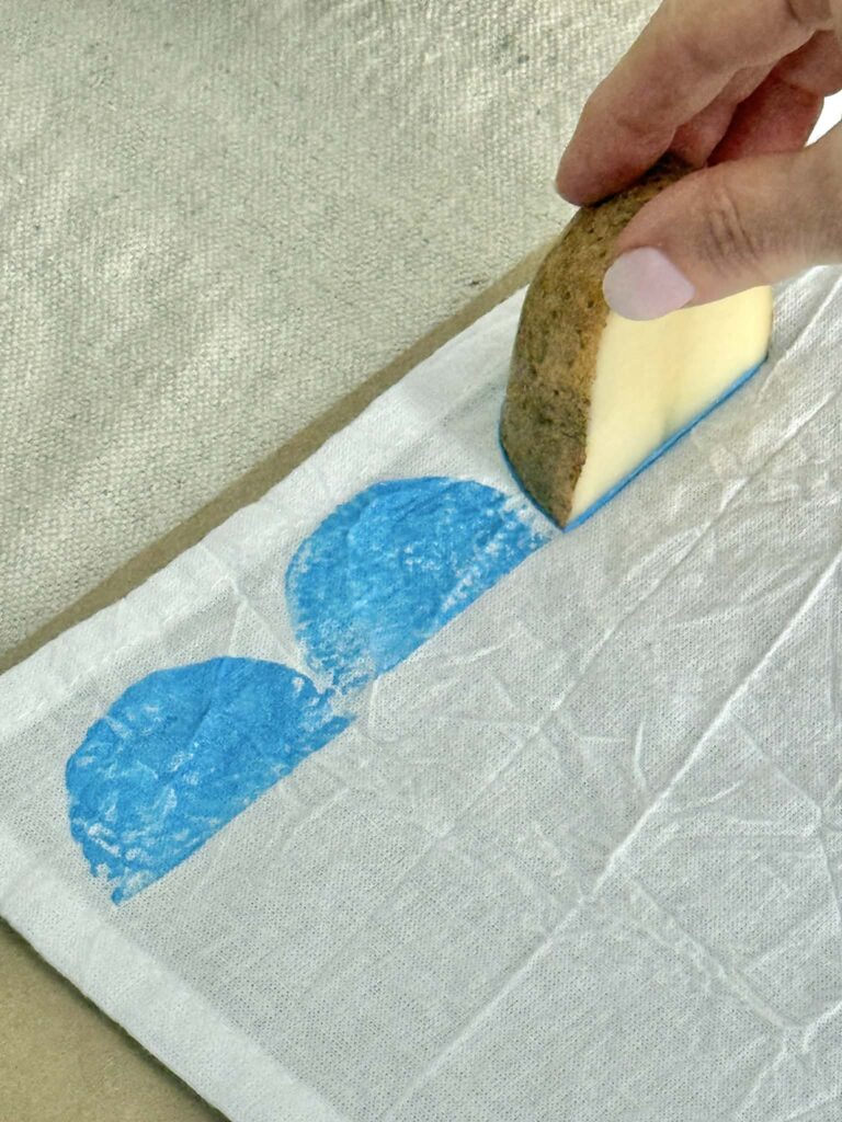 potato printing a blue half moon pattern on a tea towel.