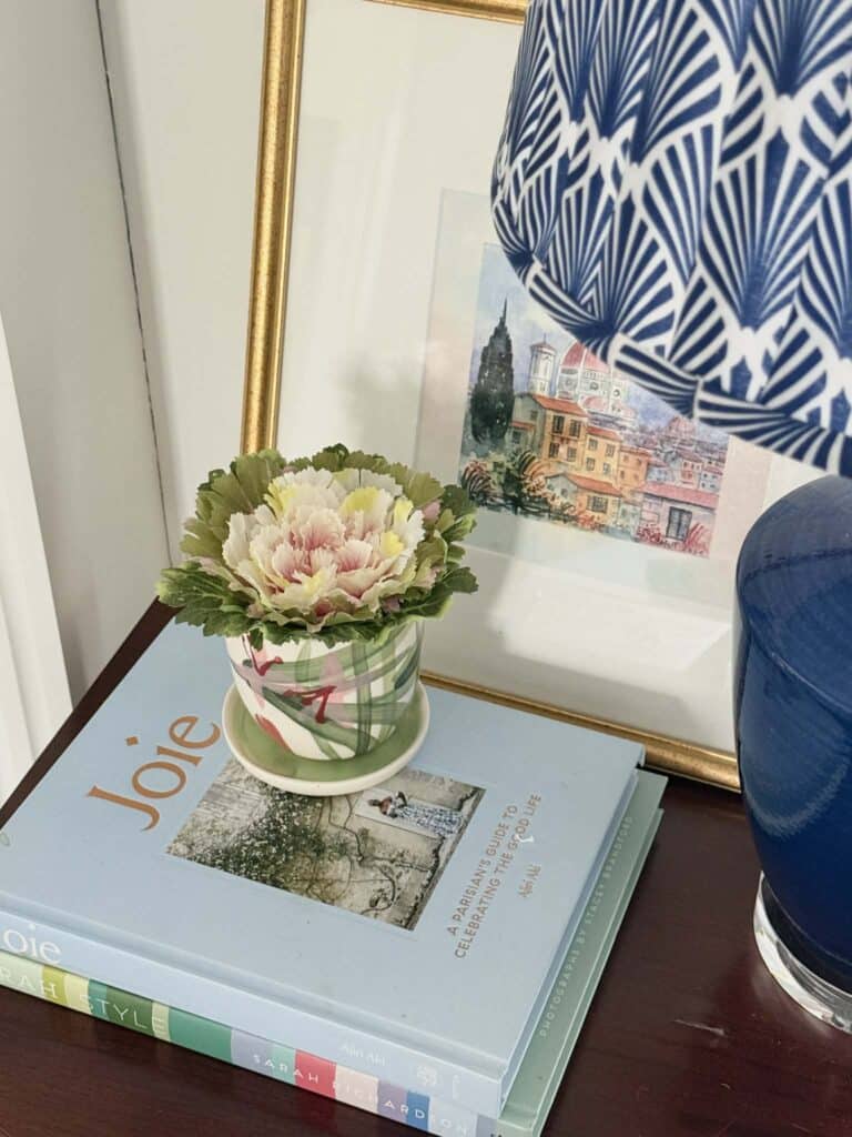 A faux cabbage in a decorative pot on a stack of books.