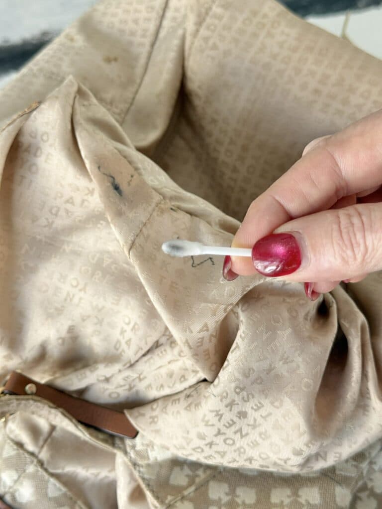 Wiping ink stains with a Q-tip and rubbing alcohol to clean a canvas bag.