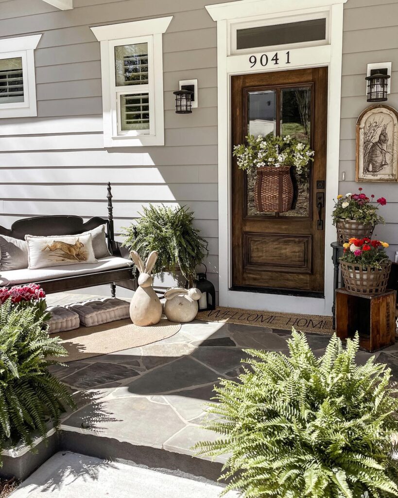 A front porch decorated with flowrs, bunnies, lanterns, and a hanging door basket.