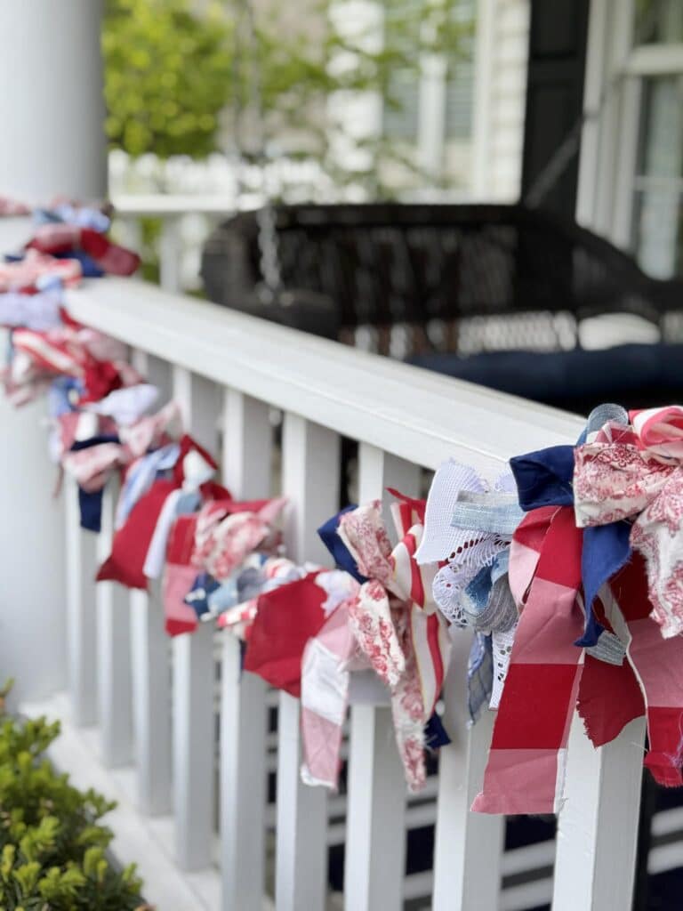 A red, white, and blue DIY fabric garland hanging from a white front porch railing.