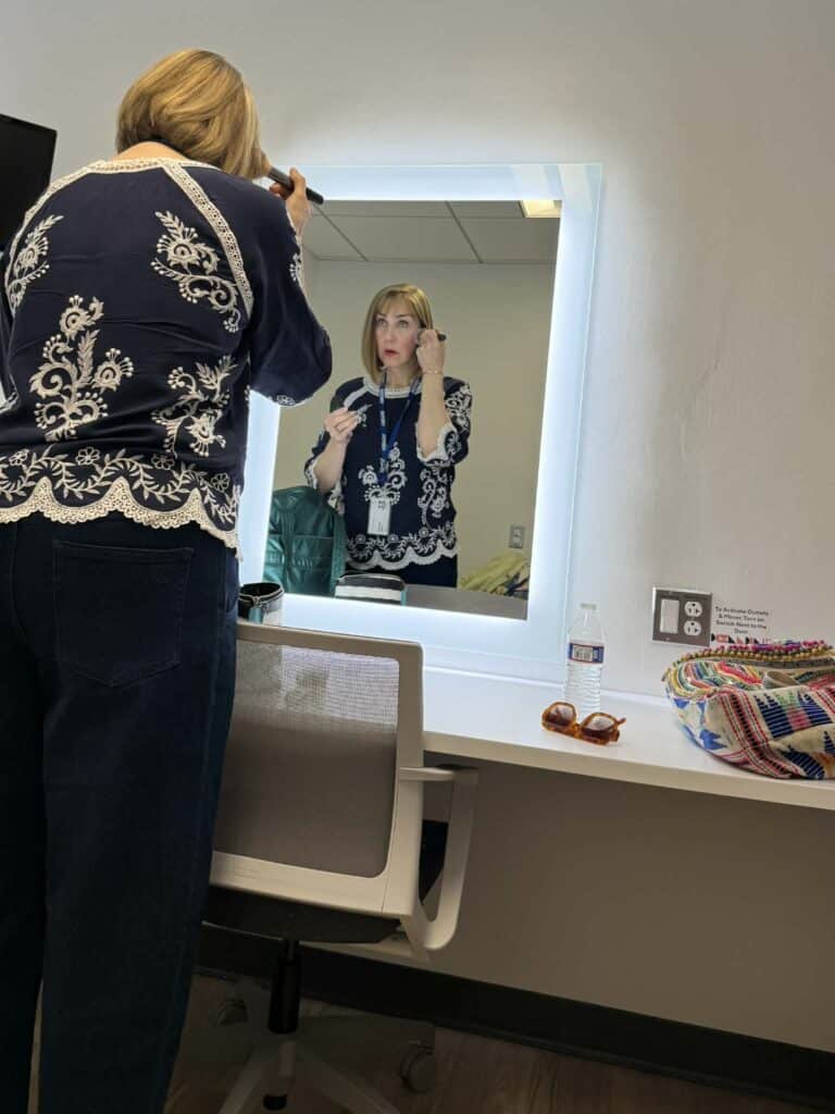 A woman putting on makeup in front of a mirre.