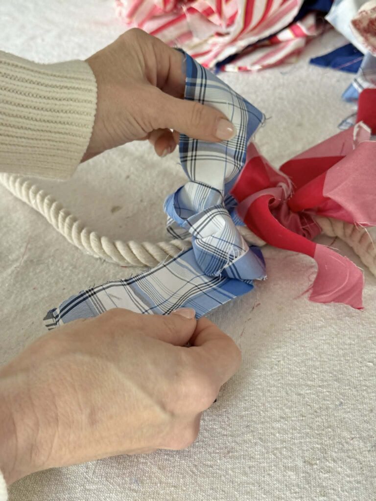 A woman's hands tying a fabric strip bow onto a piece of rope.
