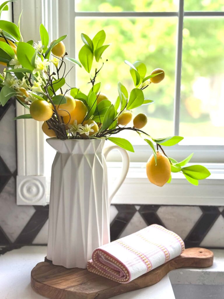 A white pitcher filled with decorative lemon branches and sitting by the kitchen sink.
