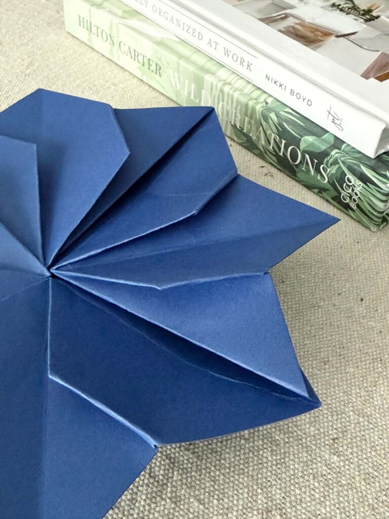 An origami envelope flower sitting beside a stack of heavy books to secure the folds.