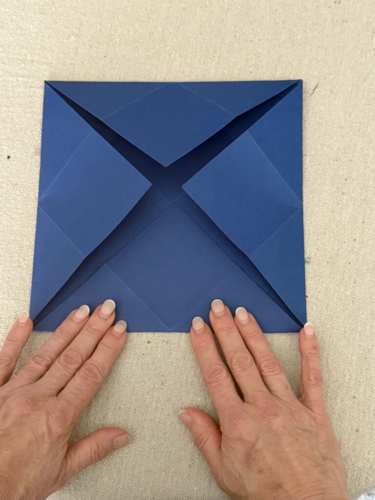 All four corners of a square piece of cardstock folded toward the center for an origami envelope.