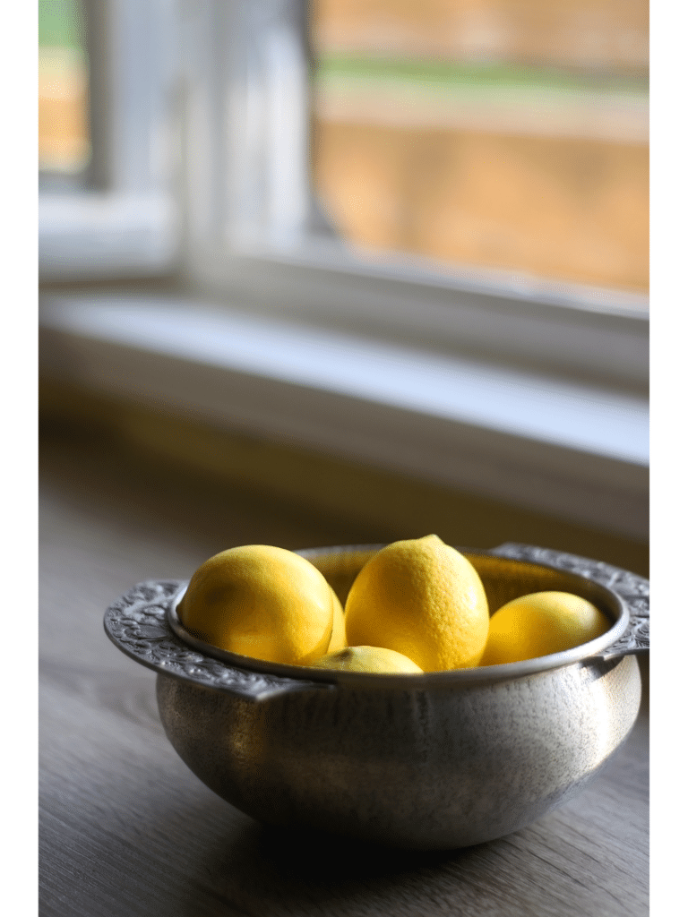 A bowl of fresh lemons sitting by a Kitchen window.
