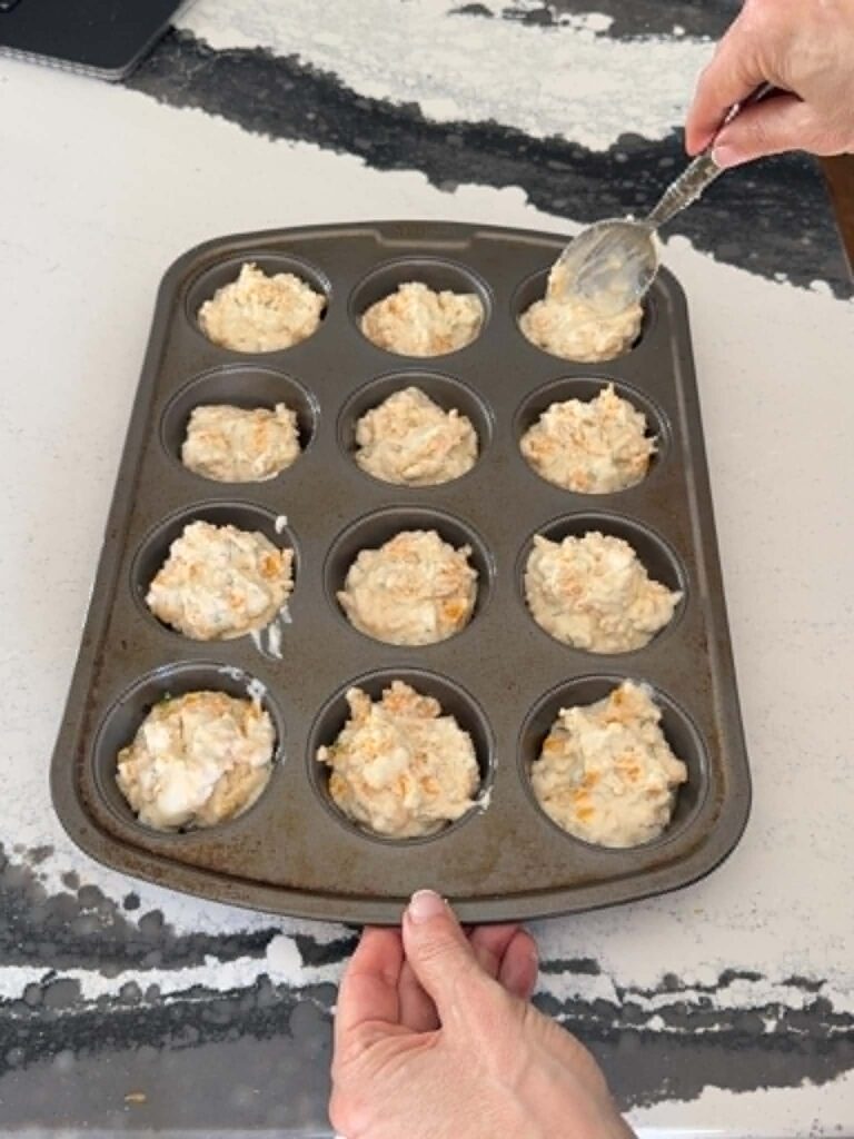 Spooning cheddar dill muffin batter into a muffin pan.