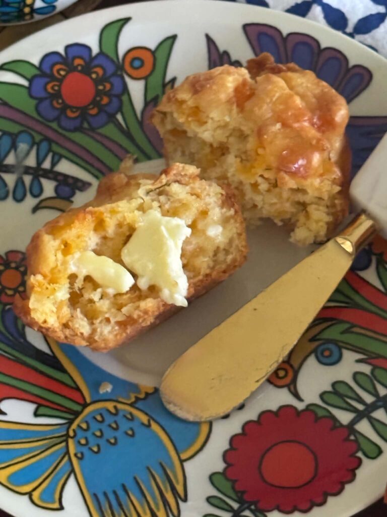 A savory cheese muffin torn in half with melting butter on top.