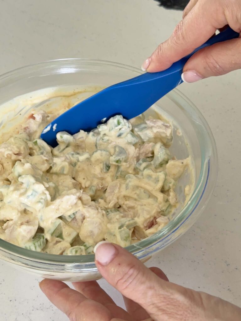 Combining the ingredients for tropical curry chicken salad with a blue spatula.