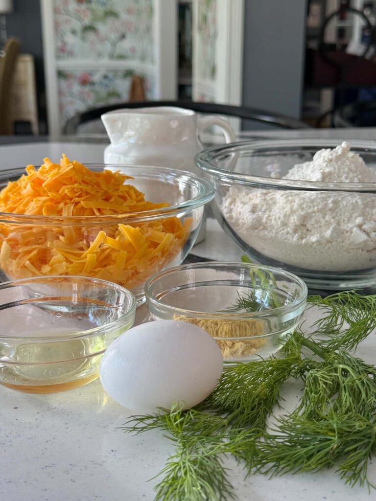 Biscuit mix, shredded cheddar cheese, milk, vegetable oil, dry mustard, an egg, and fresh dill for cheddar dill muffins.