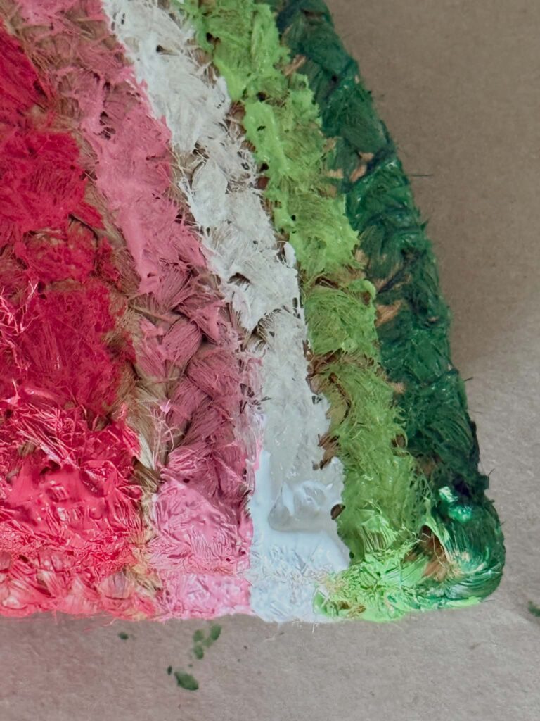 A woven placemat painted with red, pink, white, and green stripes to look like a watermelon for a door.