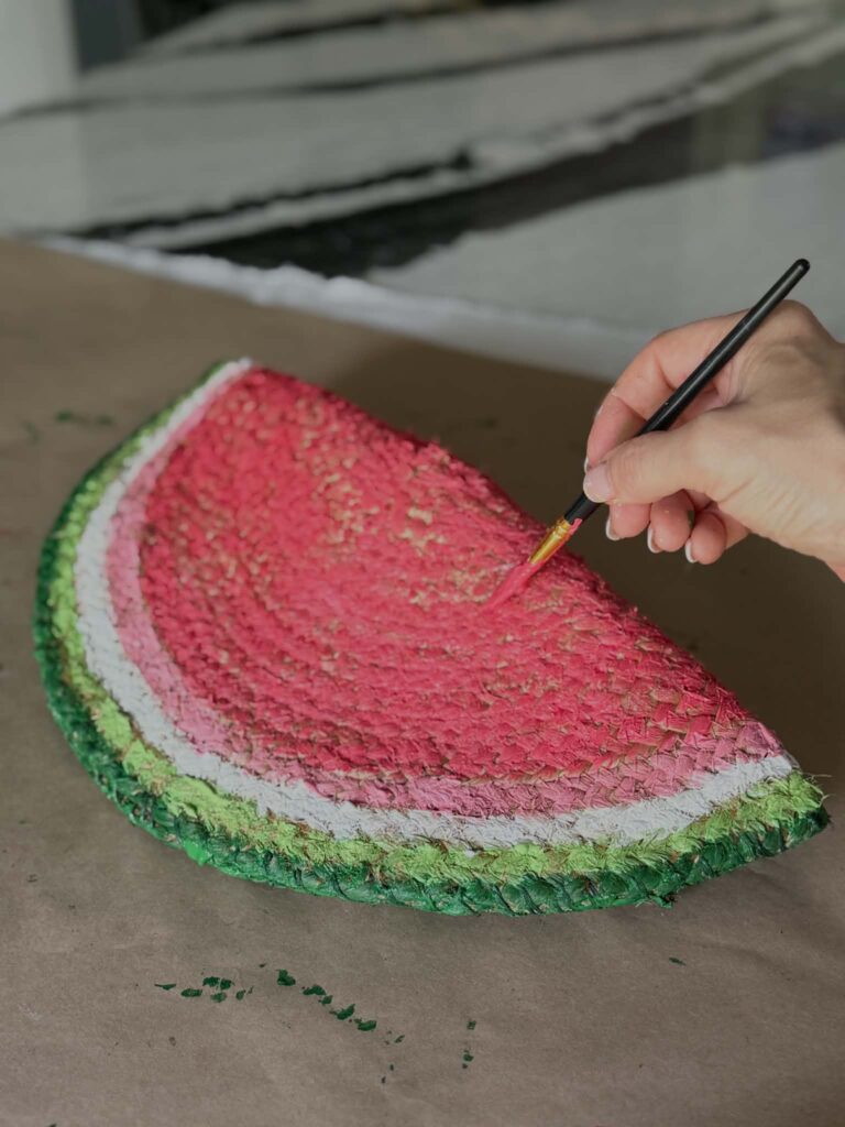 Painting the body of a watermelon door hanger diy with red paint.