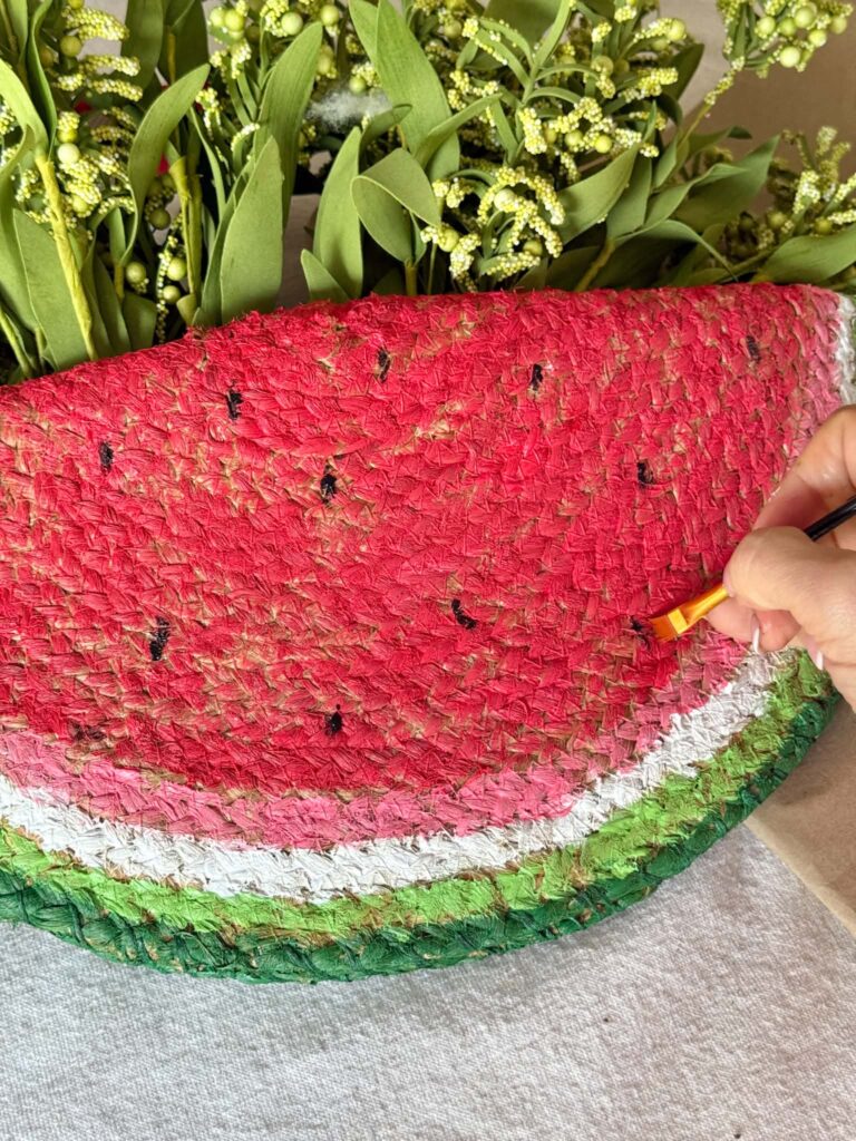 Painting black seeds onto the outside of a diy watermelon door hanger.