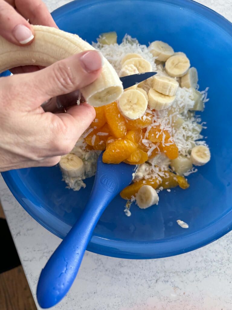 Slicing bananas into a bowl of fruit.