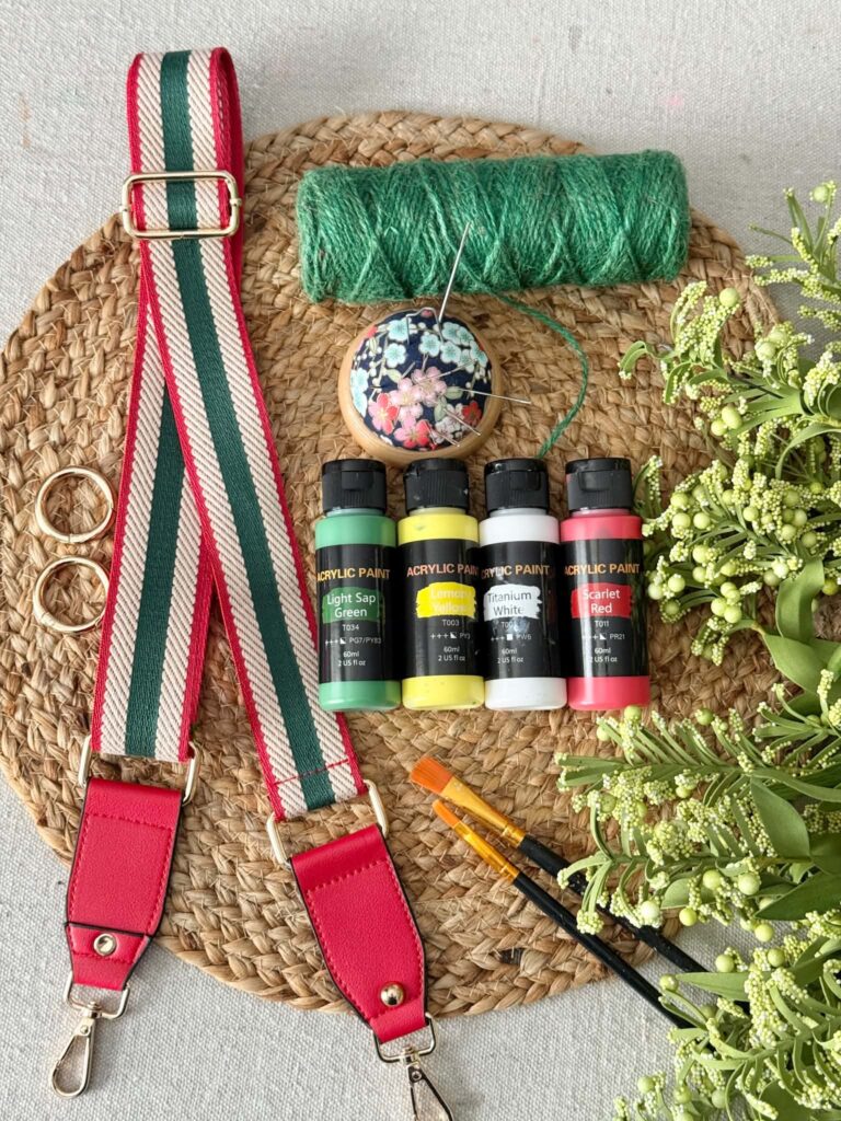 A woven placemat, guitar-style crossbody strap, green twine, paint brushes, faux greenery, and acrylic paints.