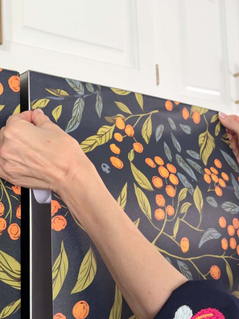 Pressing peel and stick wallpaper to a refrigerator door.