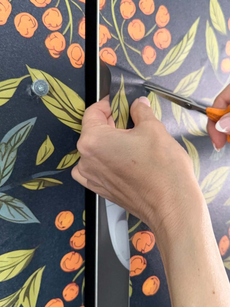 Cutting an "X" in wallpaper to make room for refrigerator door hardware bolt.