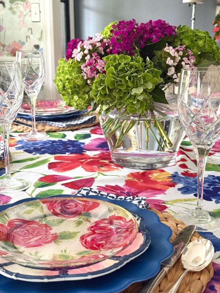 Summer tablescapes that includes floral linens, fresh flowers, and crystal goblets.