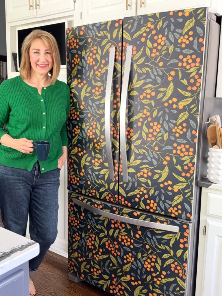 Woman holding a coffee cup and leaning against a refrigerator that has been wallpapered with peel and stick wallpaper.
