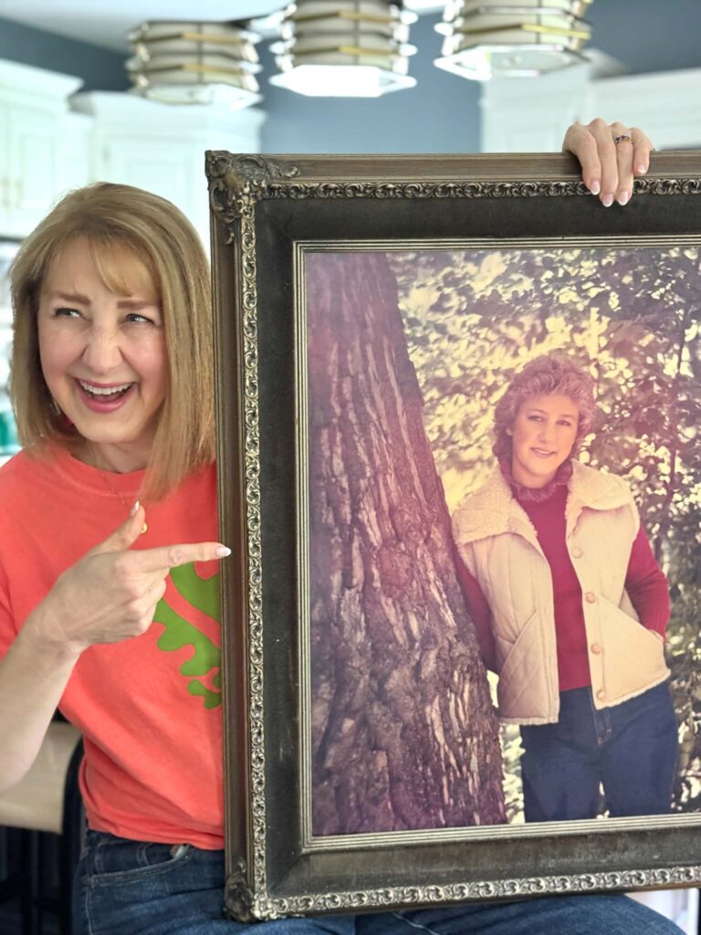 Woman laughing and pointing to an old portrait of herself.