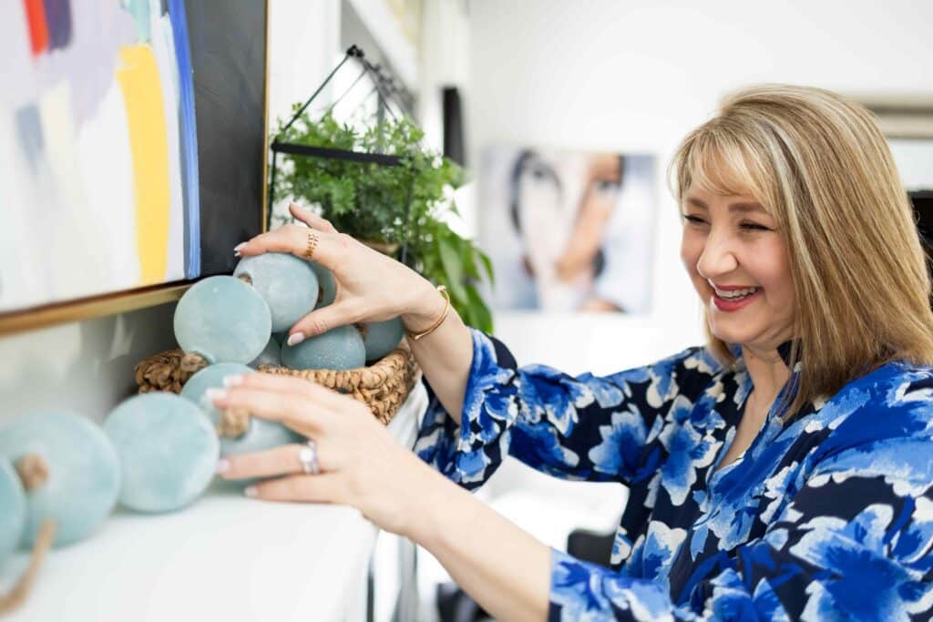 A woman slowly decorating a fireplace mantel with blue glass bead garland.