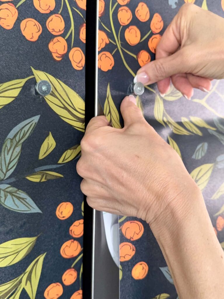 Smoothing wallpaper around refrigerator door bolt.