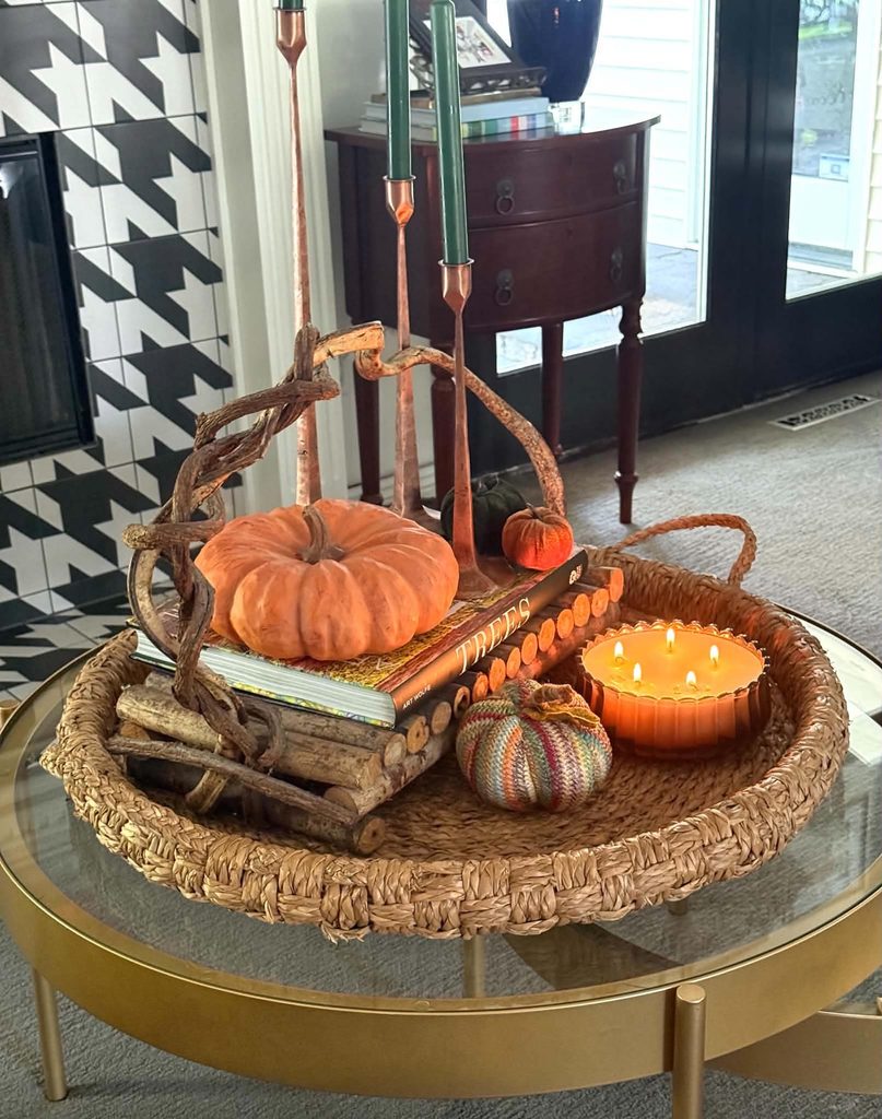 A fall tray decor idea consisting of a woven tray layered with a gnarly wood handle tray filled with books and pumpkins.