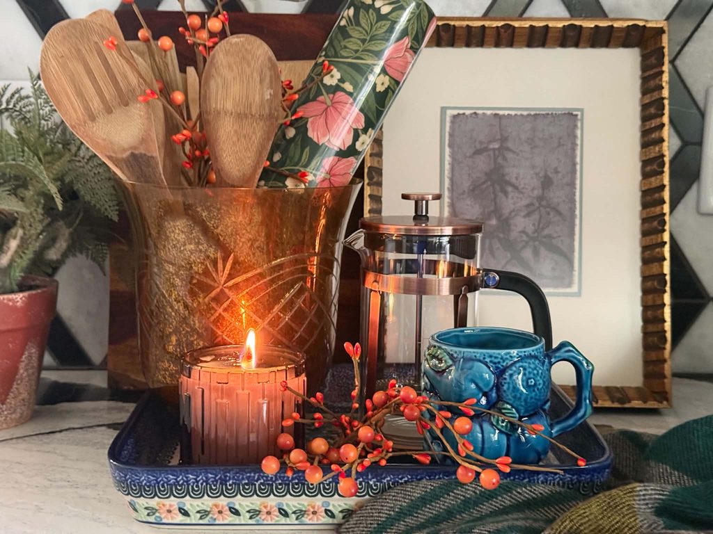A polish stoneware tray holding a french press, coffee mug, lighted candle, and container holding wooden spoons.
