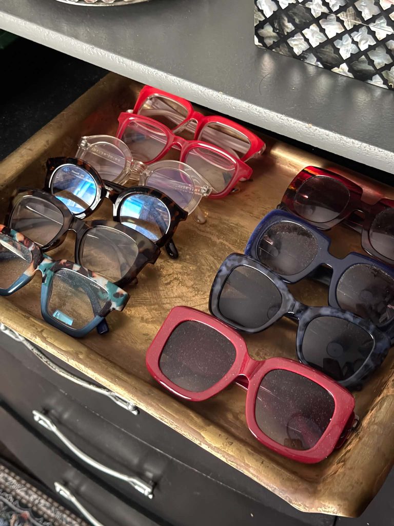 A brass tray displaying eyeglasses and sunglasses as apart of a closet vanity.
