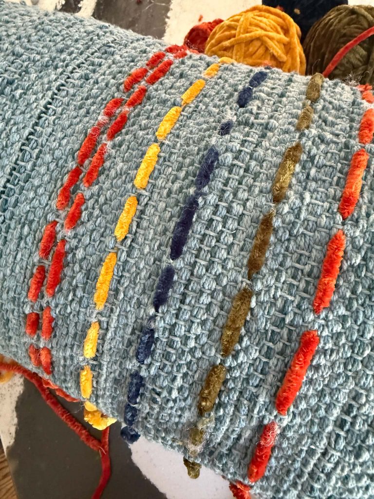 Running stitches placed vertically on a worn decorative throw pillow.