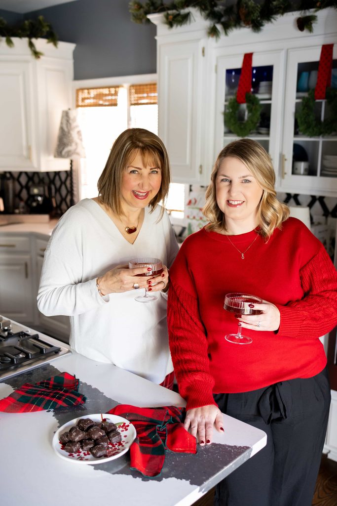 Two women, dressed for holiday entertaining, and drinking champagne cocktails.
