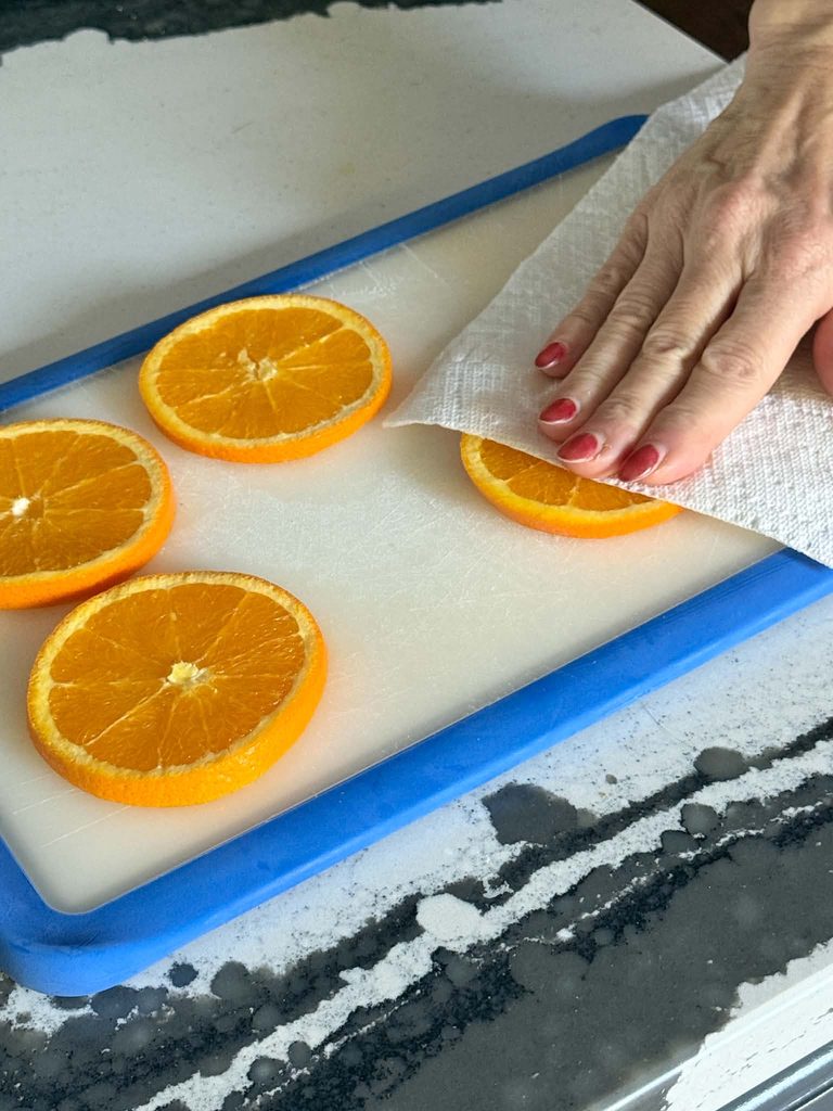 Pressing paper towel on orange slices to soak up excess juice.