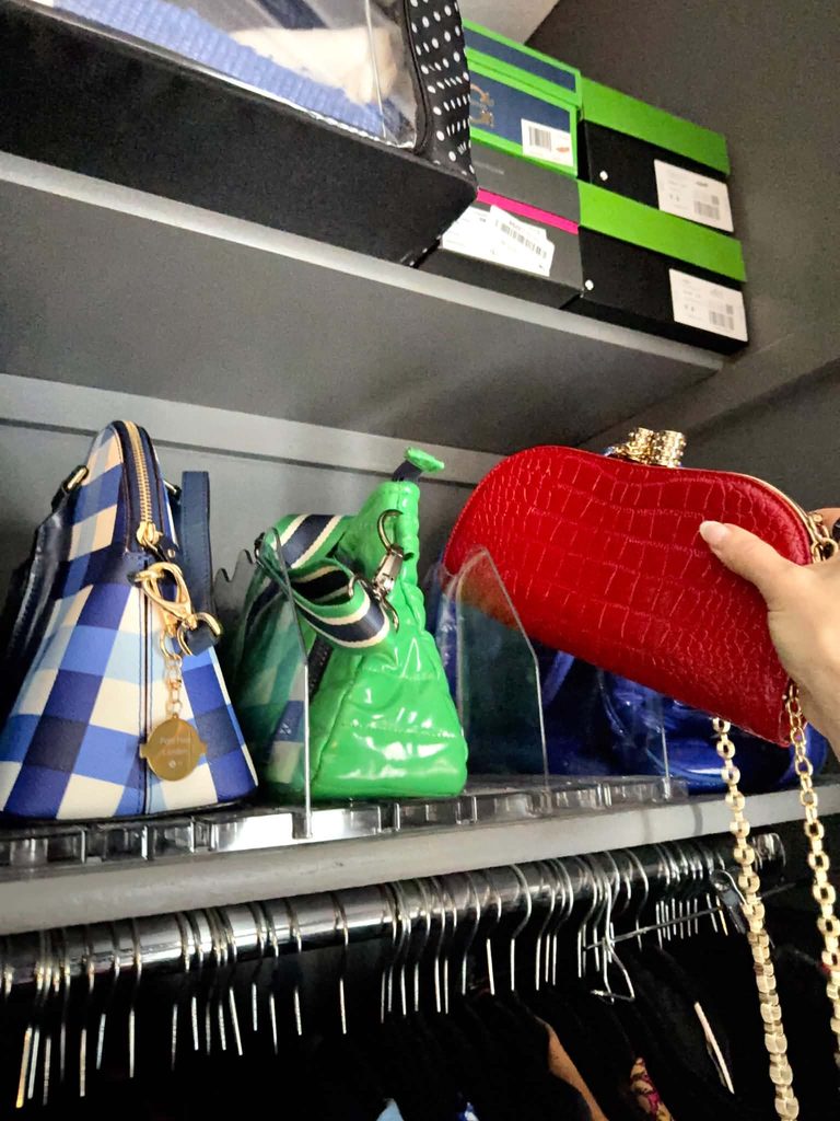 A red handbag being stored in a clear storage shelf in a small closet.