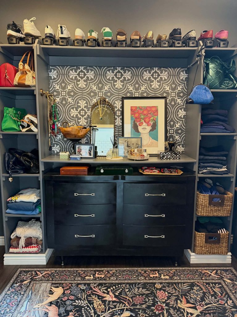 A small walk-in closet decorated with artwork, an antique mirror, a reed diffuser, storage trays and boxes.