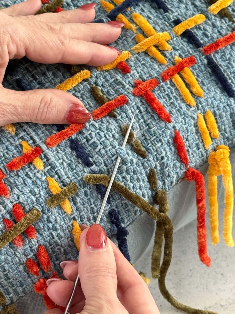 Stitching a plaid pattern on a decorative toss pillow.