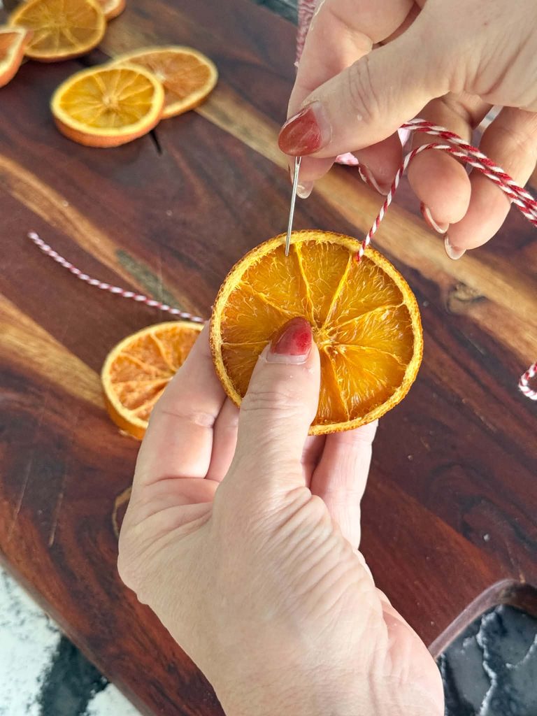 Threading a dried orange slice with twine.